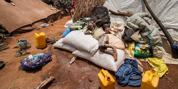 Junge aus Mosambik liegt neben Wasserkanistern auf Lebensmittelsäcken in einem Flüchtlingscamp in Malawi Junge aus Mosambik liegt neben Wasserkanistern auf Lebensmittelsäcken in einem Flüchtlingscamp in Malawi