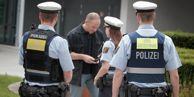 Drei Polizisten in Uniform reden mit einem Mann.