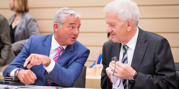 Thomas Strobl, der baden-württembergische Innenminister von der CDU beugt sich im Landtag zu Ministerpräsident Winfried Kretschmann von den Grünen