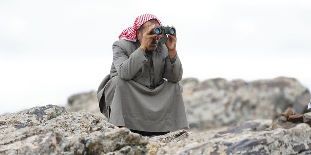 Ein türkischer Kurde hockt auf einem Felsen und schaut durch ein Fernglas Ein türkischer Kurde hockt auf einem Felsen und schaut durch ein Fernglas