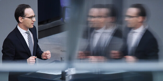 Heiko Maas steht an einem Redner_innenpult. Im gegenüber ist eine dreifache Spiegelung seiner selbst zu sehen Heiko Maas steht an einem Redner_innenpult. Im gegenüber ist eine dreifache Spiegelung seiner selbst zu sehen