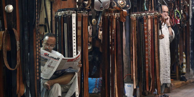 Ein Mann liest Zeitung zwischen Marktständen in Marrakesch Ein Mann liest Zeitung zwischen Marktständen in Marrakesch