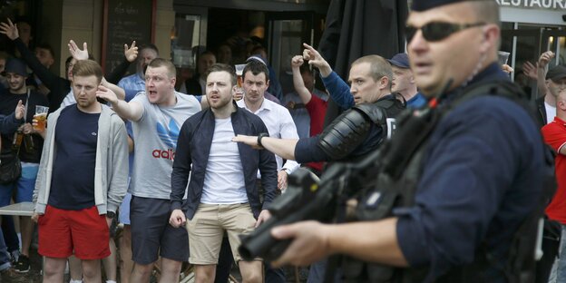 Aufgebrachte Fußballfans und ein schwerbewaffneter Polizist. Aufgebrachte Fußballfans und ein schwerbewaffneter Polizist.