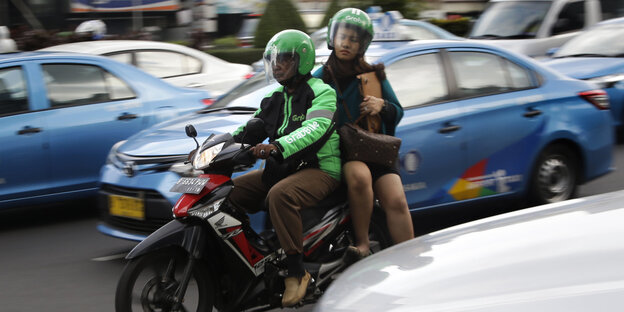 Ein Mann und eine Frau fahren auf einem Motorrad zwischen Autos Ein Mann und eine Frau fahren auf einem Motorrad zwischen Autos