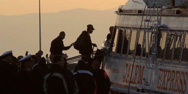 Ein Migrant wird in Griechenland von einem Frontex-Offizier auf eine Fähre eskortiert.
