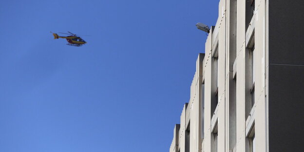 Ein Polizeihubschrauber fliegt am blauen Himmel auf einen Wohnhauskomplex zu Ein Polizeihubschrauber fliegt am blauen Himmel auf einen Wohnhauskomplex zu