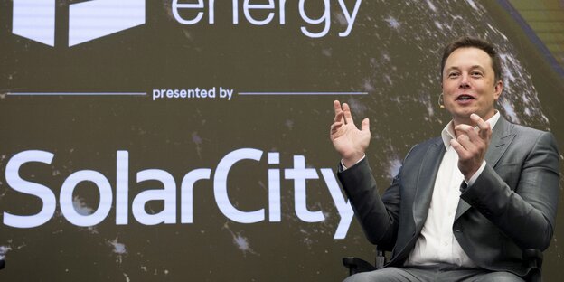 Elon Musk sitzend, vor dem Firmenlogo von SolarCity Elon Musk sitzend, vor dem Firmenlogo von SolarCity