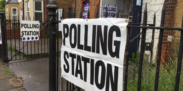An einem Zaun hängt ein Schild „Polling Station“ An einem Zaun hängt ein Schild „Polling Station“