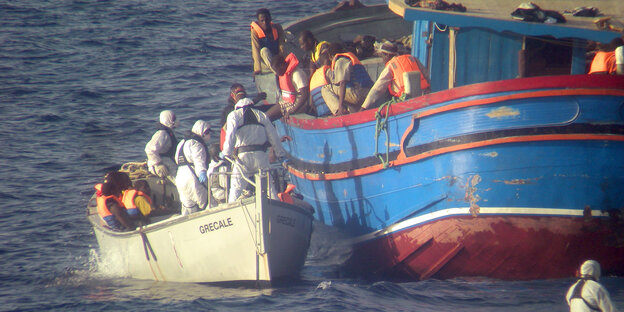 Menschen steigen von einem kleinen auf ein großes Boot Menschen steigen von einem kleinen auf ein großes Boot