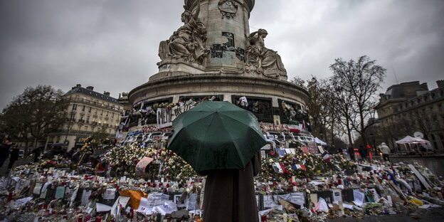 Eine Person steht mit einem Regenschirm auf dem Place de la Republique und schaut an das Denkmal für die Toten der Terroranschläge vom 13. November Eine Person steht mit einem Regenschirm auf dem Place de la Republique und schaut an das Denkmal für die Toten der Terroranschläge vom 13. November