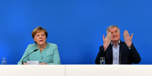 Kanzlerin Angela Merkel und CSU-Chef Horst Seehofer sitzen vor einem blauen Hintergrund