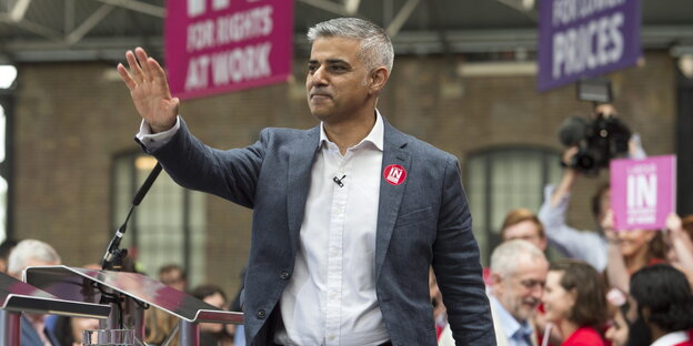 Ein Mann in Hemd und Jackett hebt die Hand zum Gruß, es ist Sadiq Khan Ein Mann in Hemd und Jackett hebt die Hand zum Gruß, es ist Sadiq Khan
