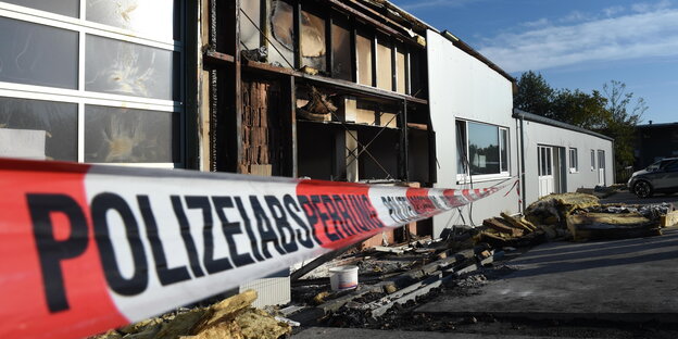 Polizei-Absperrband vor einer halb abgebrannten Halle Polizei-Absperrband vor einer halb abgebrannten Halle