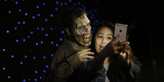 Ein Mädchen macht ein Selfie von sich und einem Mensch mit Zombiemaske