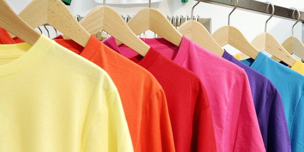 Mehrere bunte T-Shirts hängen auf Bügeln hintereinander auf einer Stange Mehrere bunte T-Shirts hängen auf Bügeln hintereinander auf einer Stange