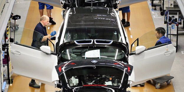Zwei Männer stehen in einer Fabrik an einem Auto Zwei Männer stehen in einer Fabrik an einem Auto