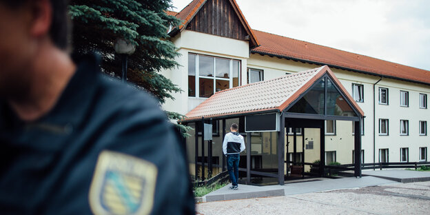 Ein Polizist steht vor einem langgestreckten Gebäude Ein Polizist steht vor einem langgestreckten Gebäude
