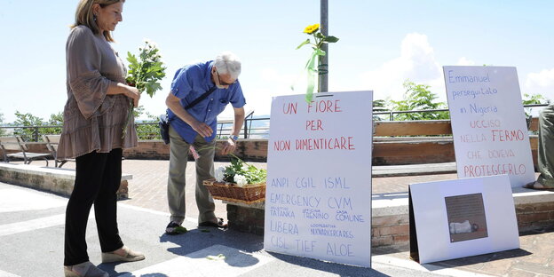 Zwei Menschen legen neben Schildern mit italienischer Aufschrift Blumen nieder Zwei Menschen legen neben Schildern mit italienischer Aufschrift Blumen nieder
