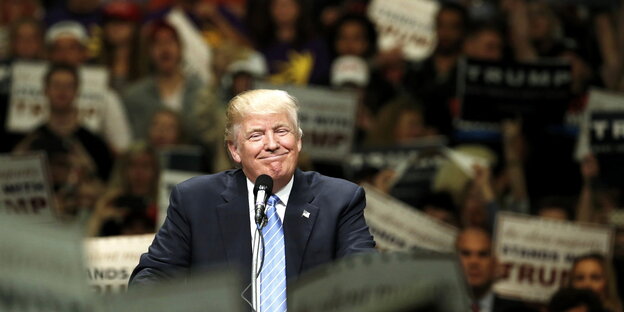 Donald Trump an einem Rednerpult, umgeben von vielen Menschen Donald Trump an einem Rednerpult, umgeben von vielen Menschen