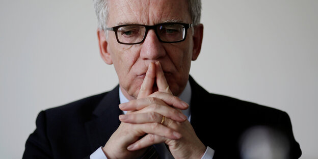 Thomas de Maizière hält die gefalteten Hände vor den Mund, die Zeigefinger zur Nase hin gestreckt Thomas de Maizière hält die gefalteten Hände vor den Mund, die Zeigefinger zur Nase hin gestreckt
