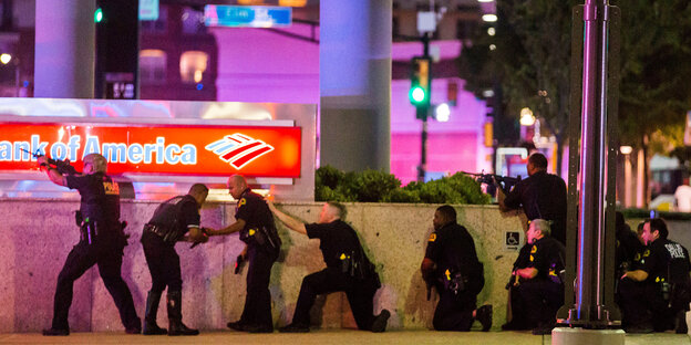 US-Polizisten stehen und hocken in einer Reihe hinter einer Mauer der „Bank of America“ US-Polizisten stehen und hocken in einer Reihe hinter einer Mauer der „Bank of America“
