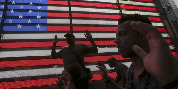 Vor dem Hintergrund einer US-Flagge gehen Menschen mit erhobenen Händen Vor dem Hintergrund einer US-Flagge gehen Menschen mit erhobenen Händen