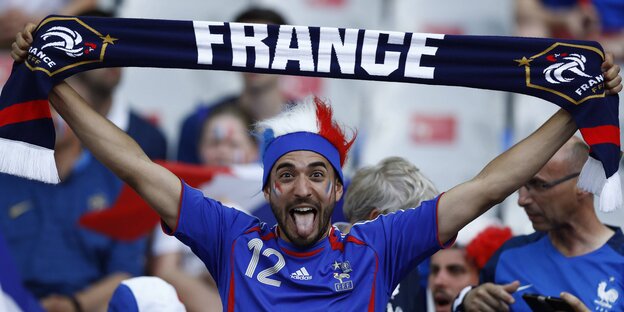 Französischer Fan streckt die Zunge raus und hält einen Schal in die Luft Französischer Fan streckt die Zunge raus und hält einen Schal in die Luft