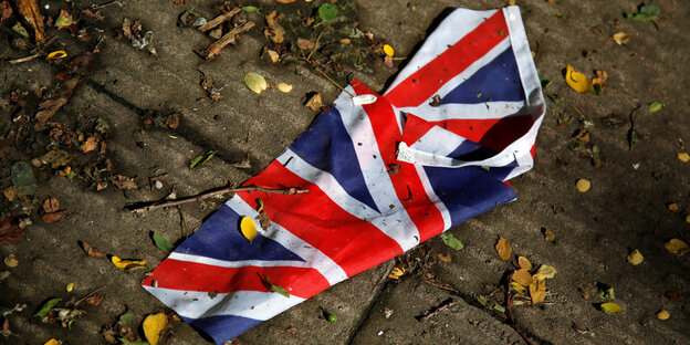 Eine britische Flagge liegt auf dem Boden zwischen Blättern und Ästen Eine britische Flagge liegt auf dem Boden zwischen Blättern und Ästen