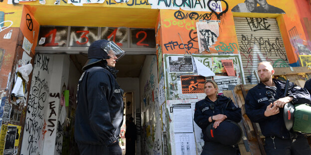 Polizisten in Schutzkleidung stehen vor einem bunt angemalten Haus