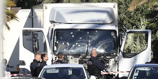 Ein Lkw mit Einschüssen in der Frontscheibe steht hinter anderen Autos. Sicherheitskräfte stehen davor.