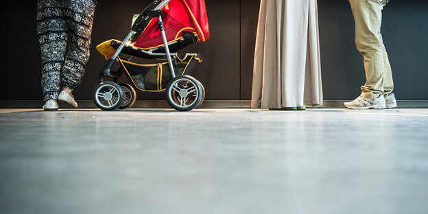Beine von wartenden Menschen, dazwischen steht ein Kinderwagen Beine von wartenden Menschen, dazwischen steht ein Kinderwagen