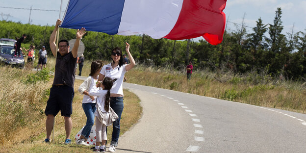 Menschen halten die französische Nationalflagge, während sie am Straßenrand stehen Menschen halten die französische Nationalflagge, während sie am Straßenrand stehen