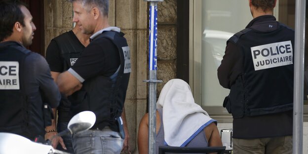 Französische Polizisten stehen um einen Mann, der ein Handtuch auf dem Kopf trägt Französische Polizisten stehen um einen Mann, der ein Handtuch auf dem Kopf trägt