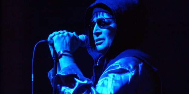 Alan Vega im Halbdunkel an einem Mikrofon Alan Vega im Halbdunkel an einem Mikrofon