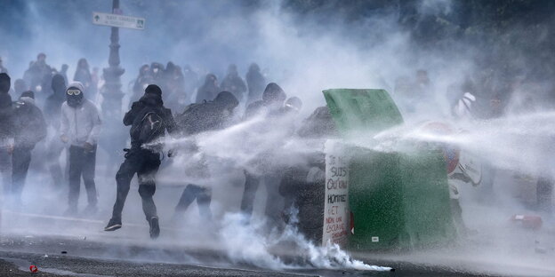 Demonstranten schützen sich vor den Strahlen eines Wasserwerfers, in dem sie sich hinter einem Müllcontainer verbergen Demonstranten schützen sich vor den Strahlen eines Wasserwerfers, in dem sie sich hinter einem Müllcontainer verbergen