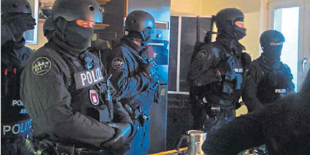 mehrere vermummte Polizisten stehen in einem Zimmer herum mehrere vermummte Polizisten stehen in einem Zimmer herum