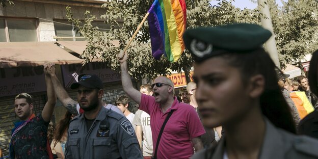 Eine Polizistin läuft neben Pride-Teilnehmer_innen. Einer hält eine Regenbogenfahne in die Höhe Eine Polizistin läuft neben Pride-Teilnehmer_innen. Einer hält eine Regenbogenfahne in die Höhe