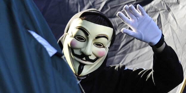Ein Mann mit Anonymous-Maske winkt in die Kamera Ein Mann mit Anonymous-Maske winkt in die Kamera