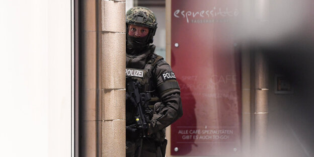Ein Polizist guckt mit einem Maschinengewehr hinter einer Wand vor Ein Polizist guckt mit einem Maschinengewehr hinter einer Wand vor