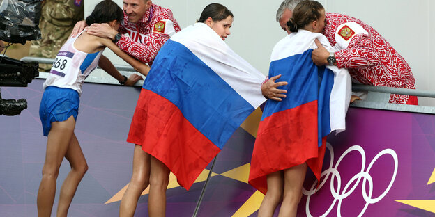 Drei Leichtathleten stehen an der Bande, zwei von ihnen haben sich die russische Nationalflagge übergehängt Drei Leichtathleten stehen an der Bande, zwei von ihnen haben sich die russische Nationalflagge übergehängt