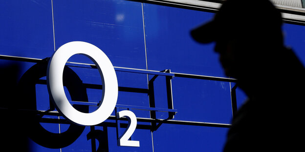 Weißer O2-Schriftzug auf blauem Grund, daneben im Vordergrund der Schatten eines Mannes Weißer O2-Schriftzug auf blauem Grund, daneben im Vordergrund der Schatten eines Mannes