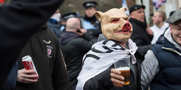 Ein Mann mit Schweinsmaske und Bier auf einer Demonstration Ein Mann mit Schweinsmaske und Bier auf einer Demonstration
