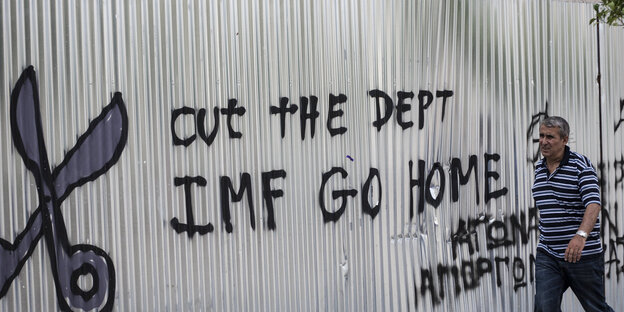 Ein Mann läuft an einer Mauer vorbei auf der "IMF go home" steht Ein Mann läuft an einer Mauer vorbei auf der "IMF go home" steht