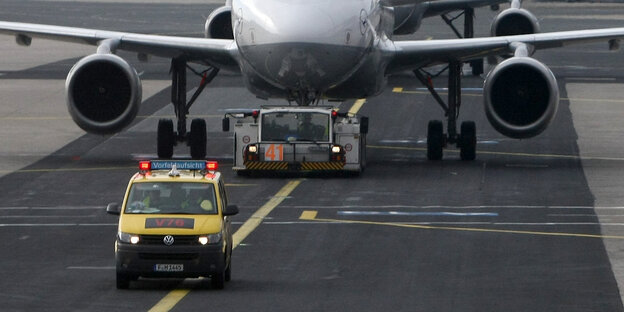 Ein gelber Kleinbus fährt auf einer Landebahn, dahinter ein Flugzeug Ein gelber Kleinbus fährt auf einer Landebahn, dahinter ein Flugzeug