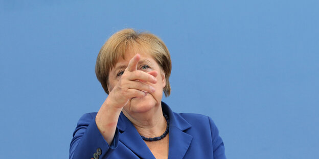 Angela Merkel vor einer blauen Wand, sie zeigt nach vorne Angela Merkel vor einer blauen Wand, sie zeigt nach vorne