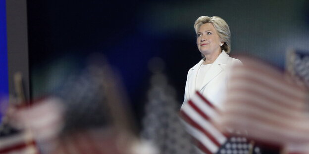 Hillary Clinton auf einer Bühne, im Vordergrund US-Fähnchen Hillary Clinton auf einer Bühne, im Vordergrund US-Fähnchen