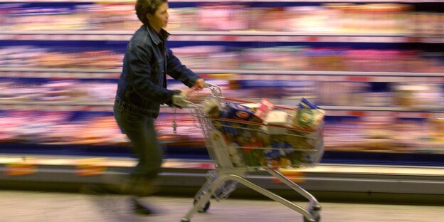 Eine Frau schiebt im Eiltempo ihren Einkaufswagen am Kühlregal vorbei Eine Frau schiebt im Eiltempo ihren Einkaufswagen am Kühlregal vorbei