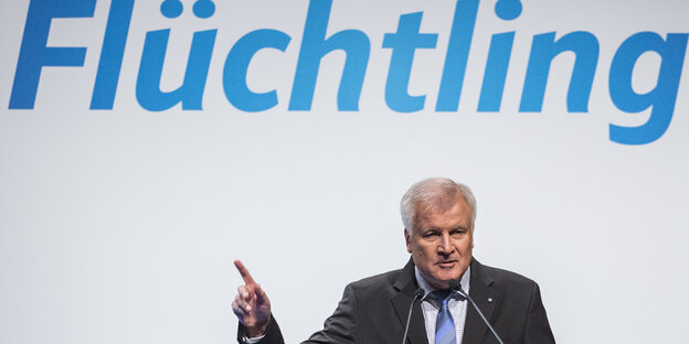 Horst Seehofer steht unter übergroßen Lettern, die das Wort Flüchtling bilden Horst Seehofer steht unter übergroßen Lettern, die das Wort Flüchtling bilden