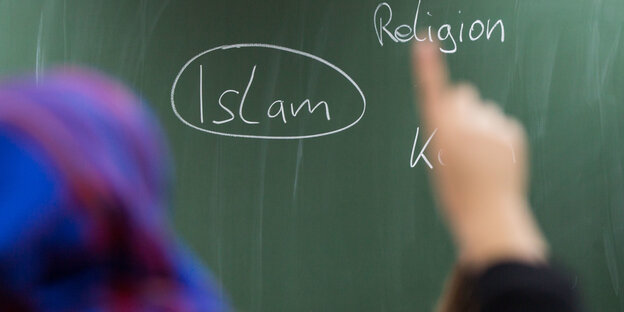 Mädchen mit Kopftuch meldet sich, vor ihr eine Tafel, auf der Islam steht Mädchen mit Kopftuch meldet sich, vor ihr eine Tafel, auf der Islam steht