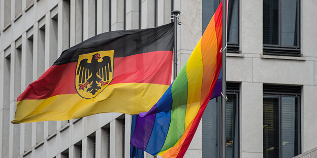 eine Deutschlandflagge und eine Regenbogenflagge wehen im Wind vor einem Gebäude eine Deutschlandflagge und eine Regenbogenflagge wehen im Wind vor einem Gebäude
